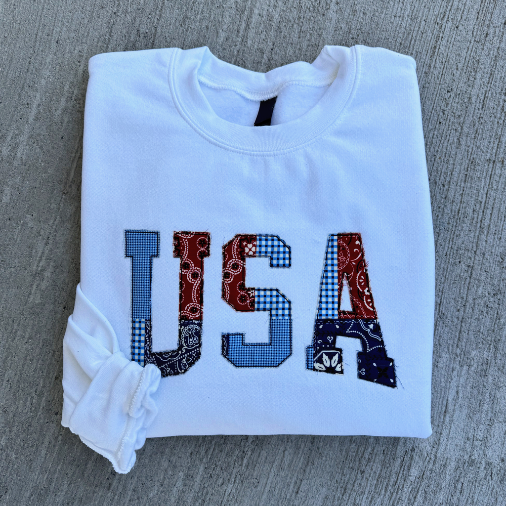 White sweatshirt with 'USA' patterned letters design on a gray surface