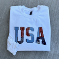 White sweatshirt with 'USA' patterned letters design on a gray surface