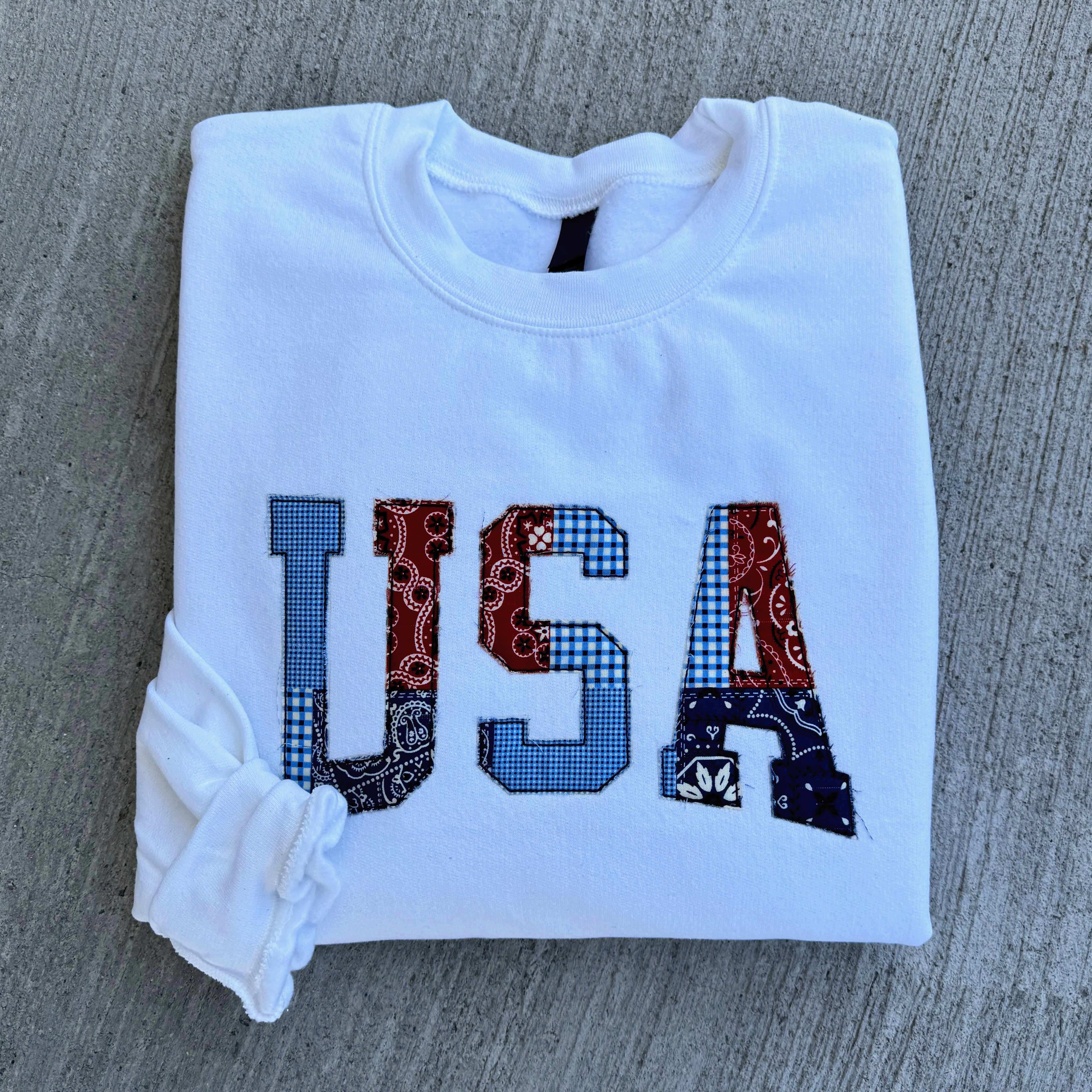 White sweatshirt with 'USA' patterned letters design on a gray surface