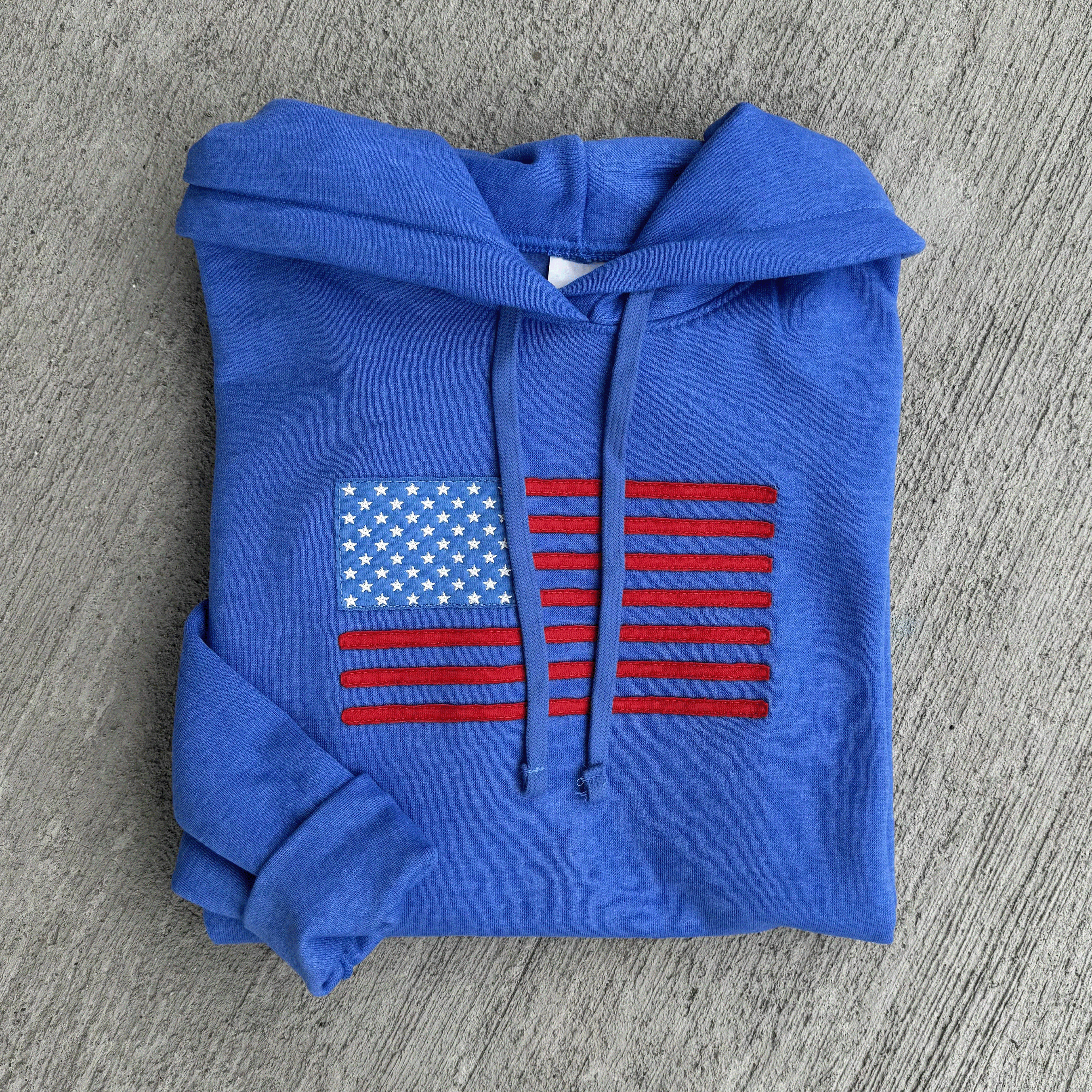 Blue hoodie with American flag design on a gray surface