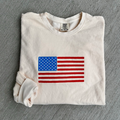 Folded off white sweatshirt with American flag design on a gray surface