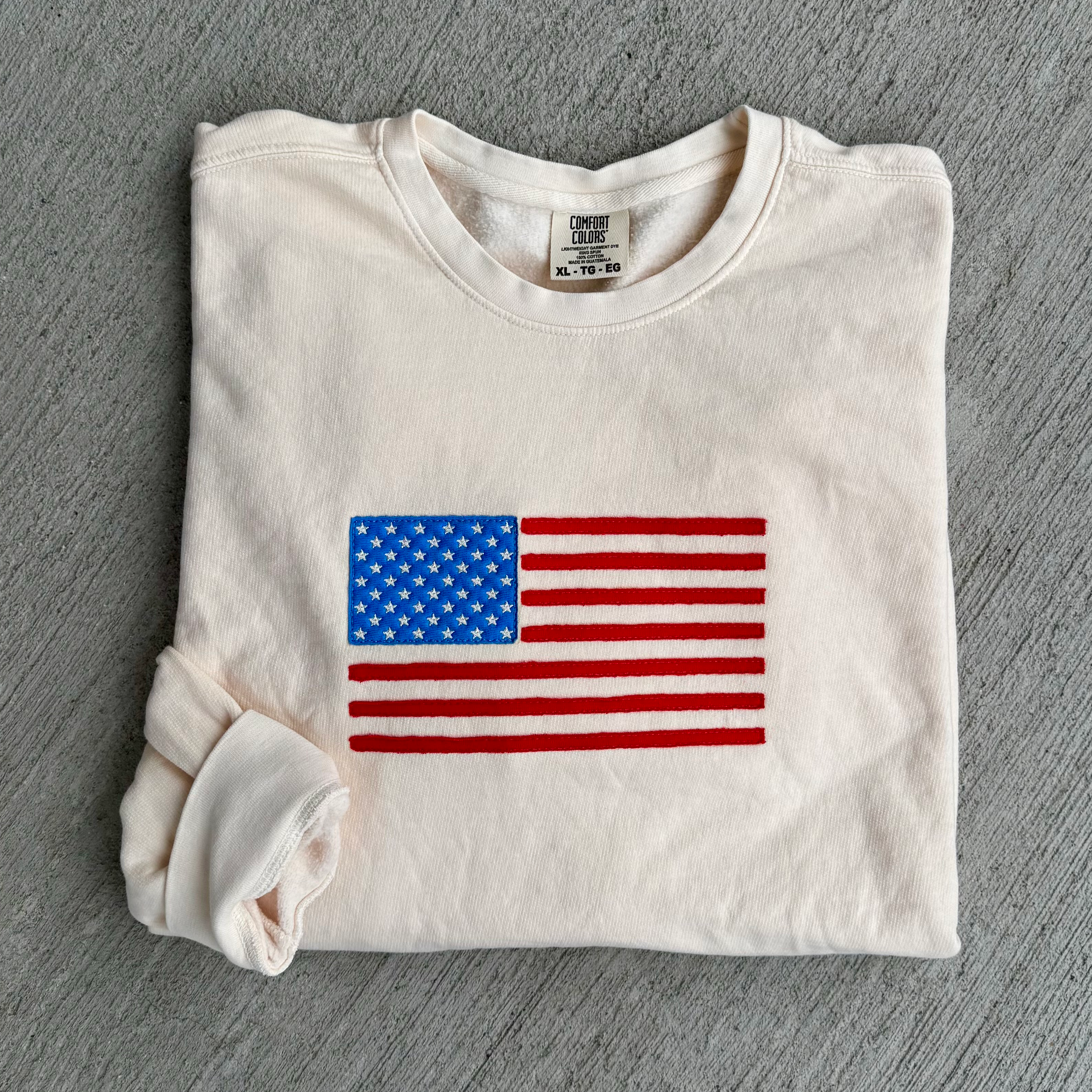 Folded off white sweatshirt with American flag design on a gray surface