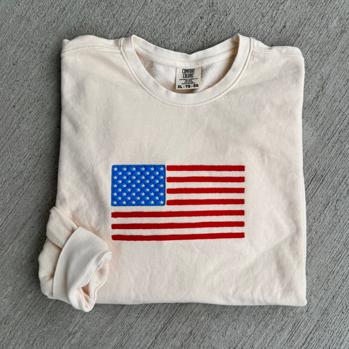Folded off white sweatshirt with American flag design on a gray surface