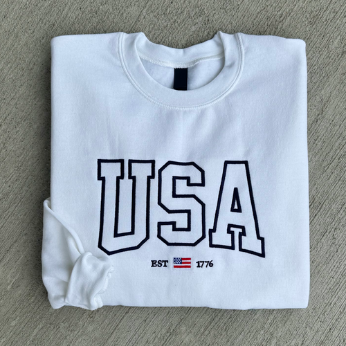 Folded white sweatshirt with 'USA' and flag design on a gray surface