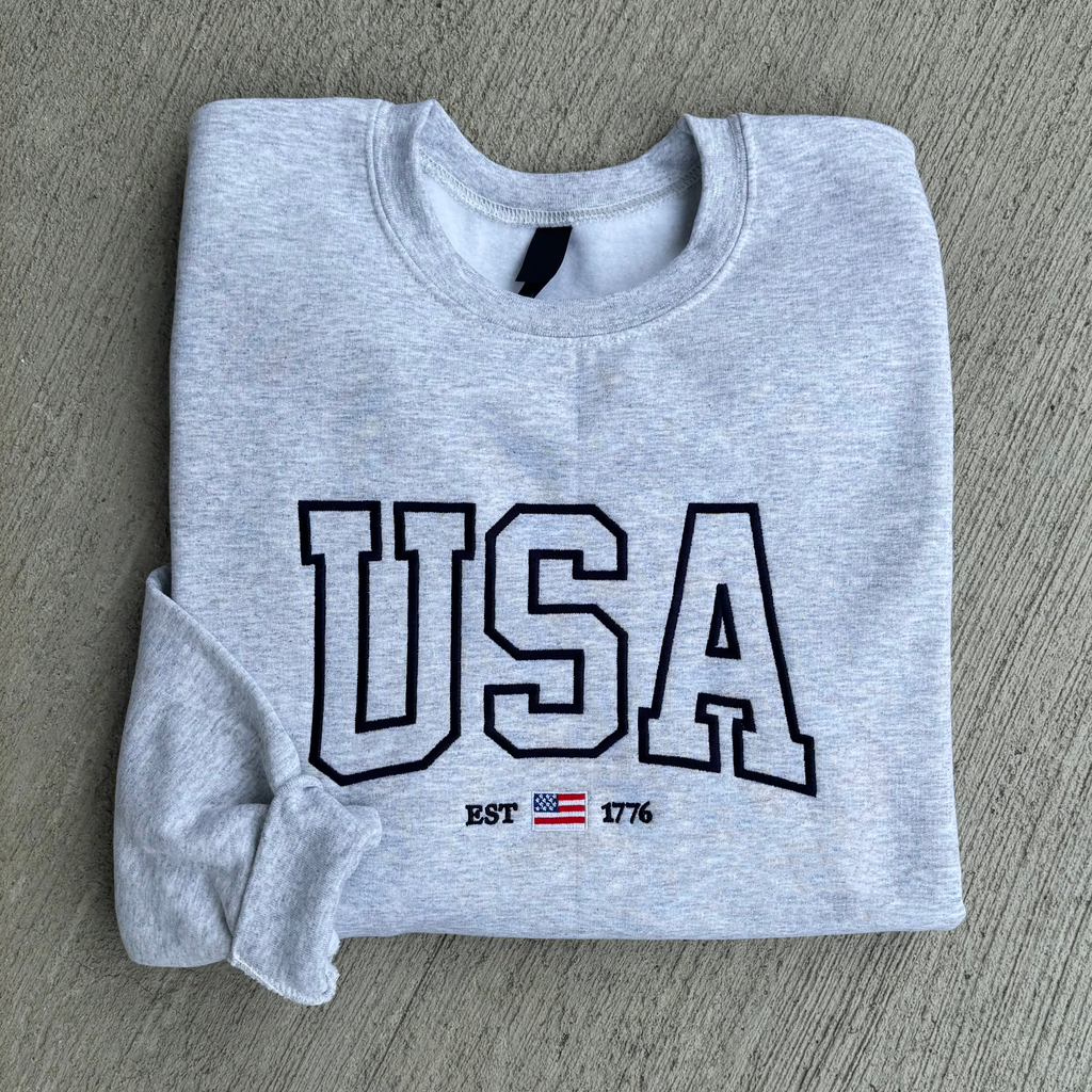Folded gray sweatshirt with 'USA' text and flag on a gray surface
