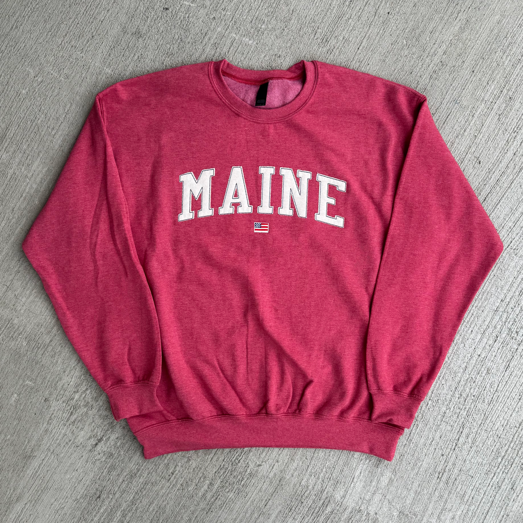 Red sweatshirt with 'MAINE' fabric embroidered on it on a gray surface