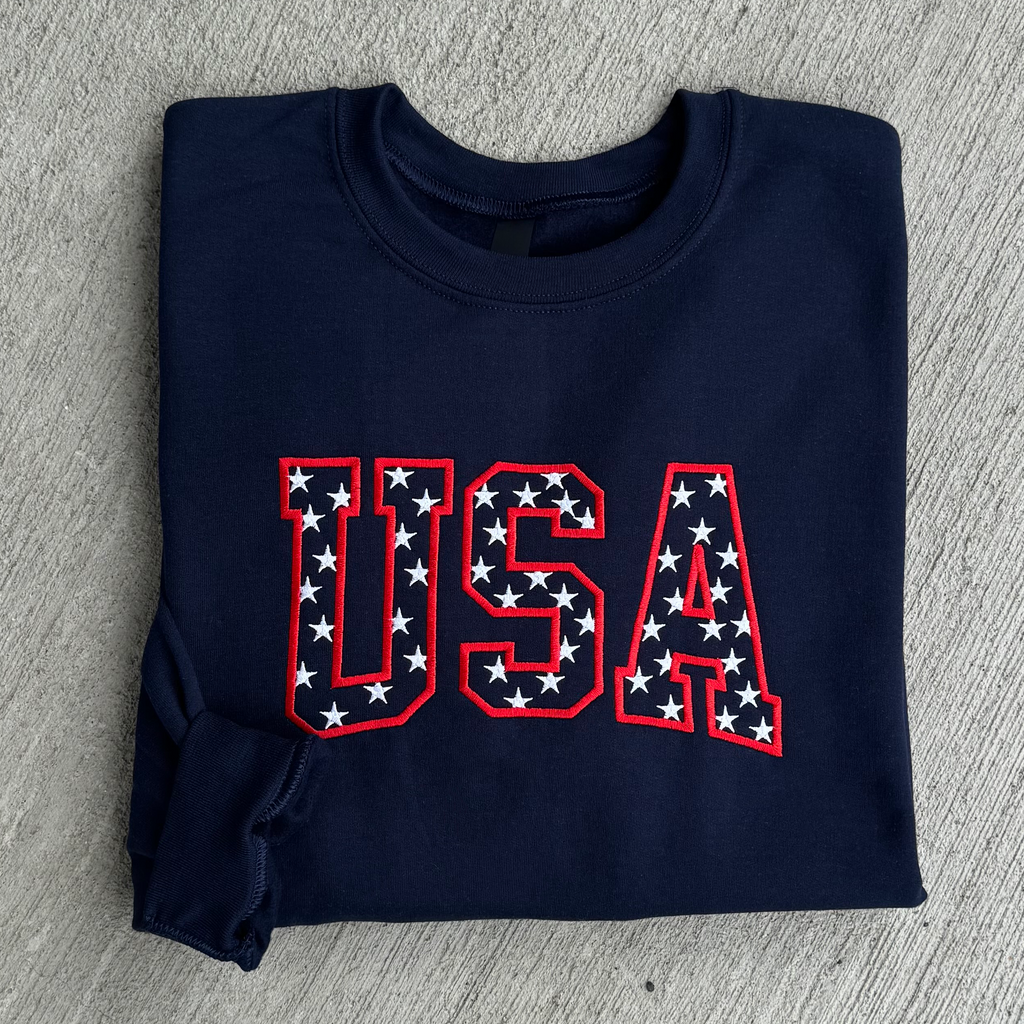 Folded navy blue sweatshirt with 'USA' text in red and white stars on a gray surface
