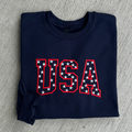 Folded navy blue sweatshirt with 'USA' text in red and white stars on a gray surface
