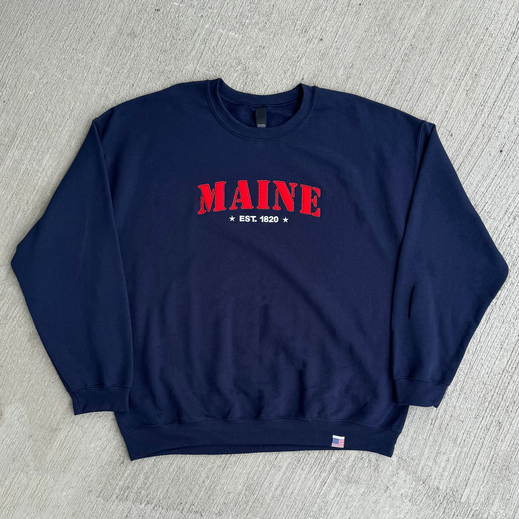 Navy blue sweatshirt with 'MAINE EST. 1820' text on a gray textured background