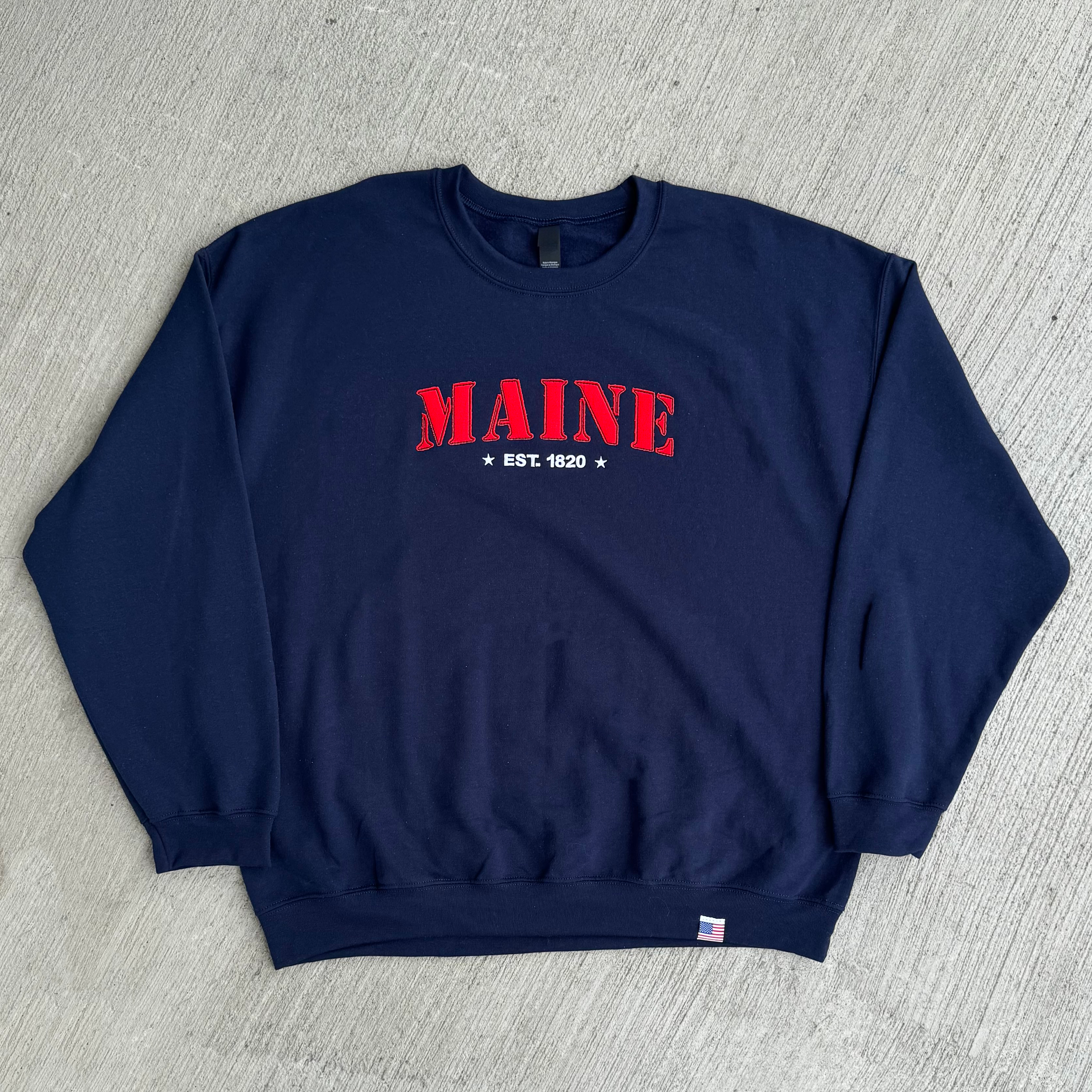 Navy blue sweatshirt with 'MAINE EST. 1820' text on a gray textured background