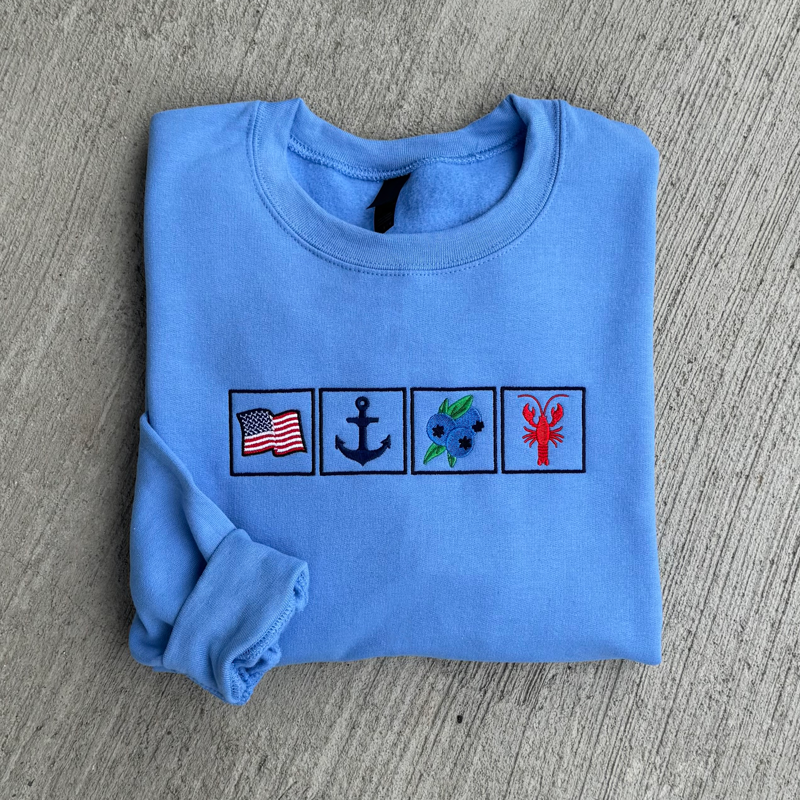 Folded blue sweatshirt with four embroidered symbols on a gray surface