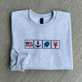 Folded gray sweatshirt with embroidered symbols on a gray surface