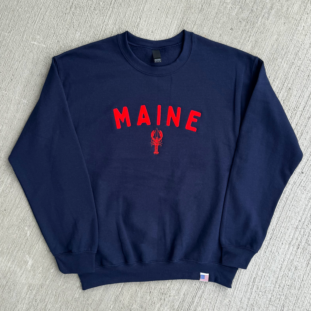 Navy blue sweatshirt with 'MAINE' and a lobster design on a gray surface