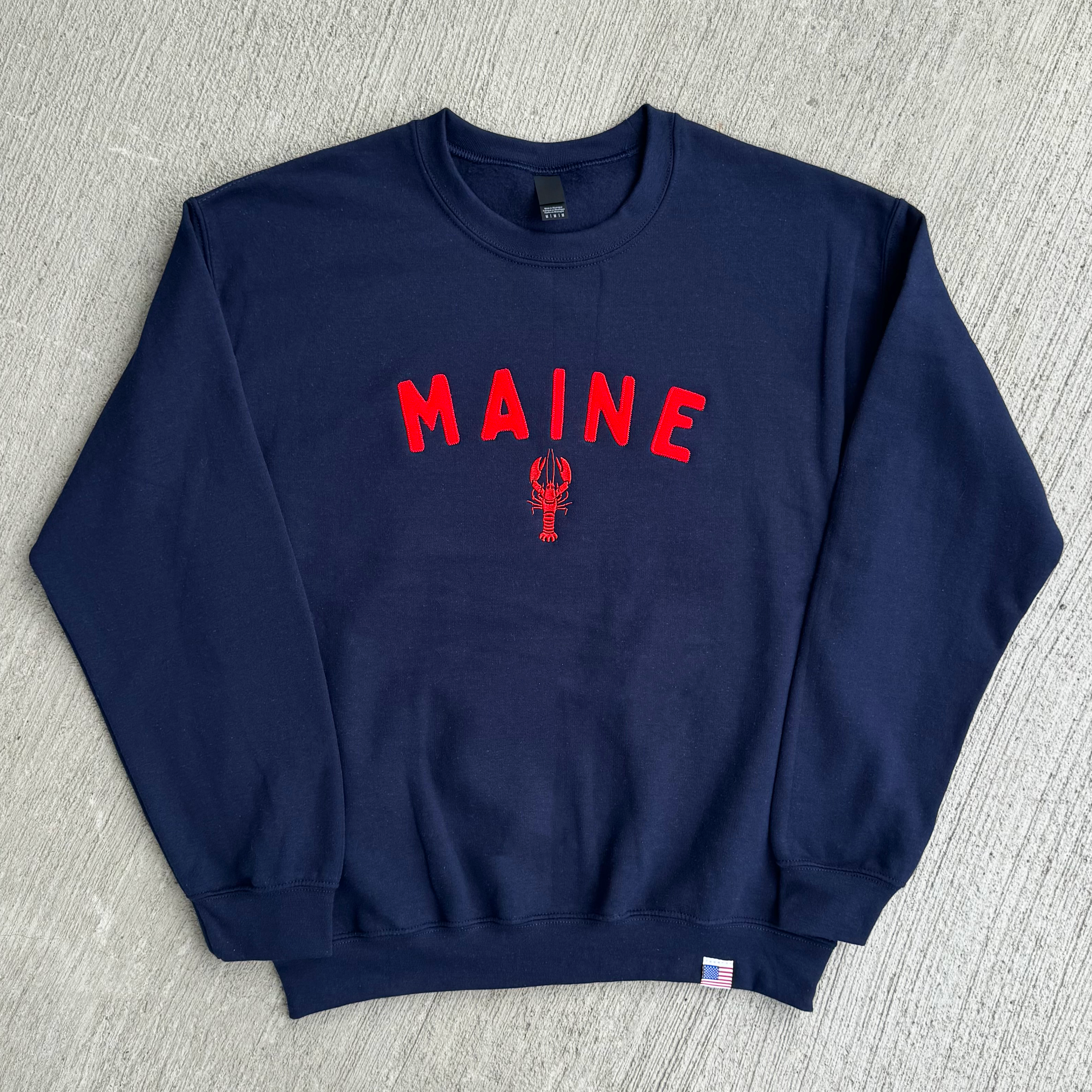 Navy blue sweatshirt with 'MAINE' and a lobster design on a gray surface