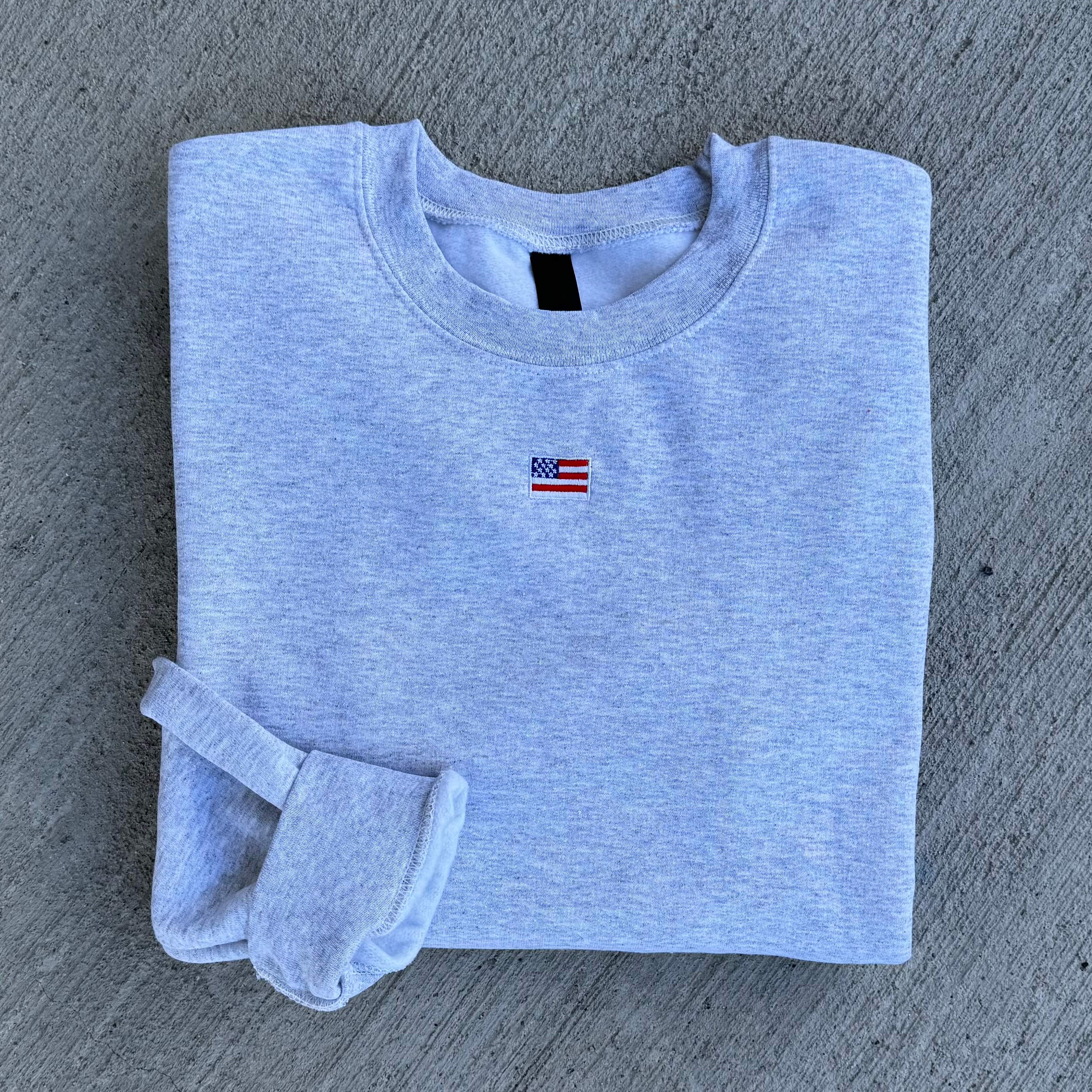 Folded gray sweatshirt with a small flag patch on a gray surface