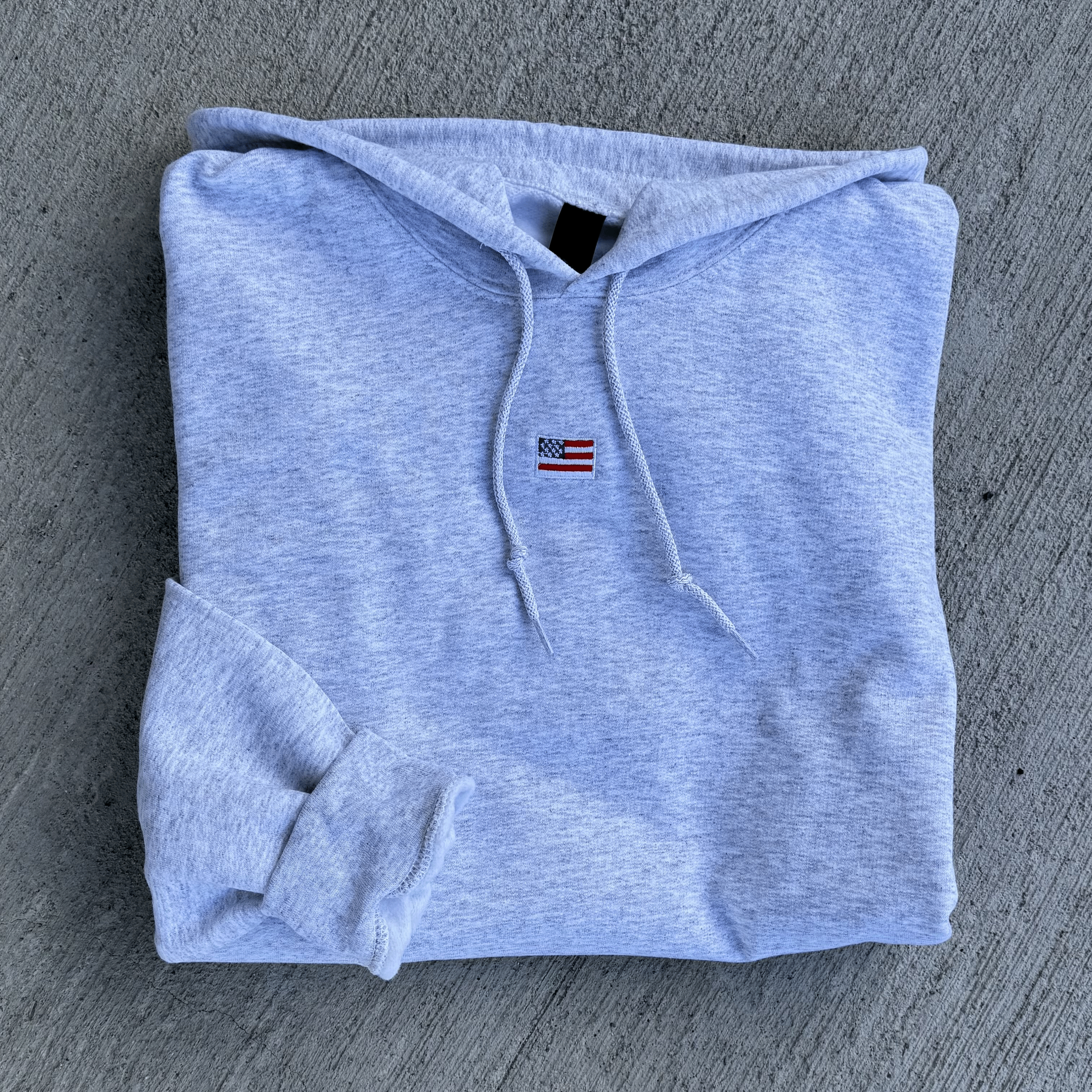 Folded gray hoodie with a small flag patch on a gray textured surface