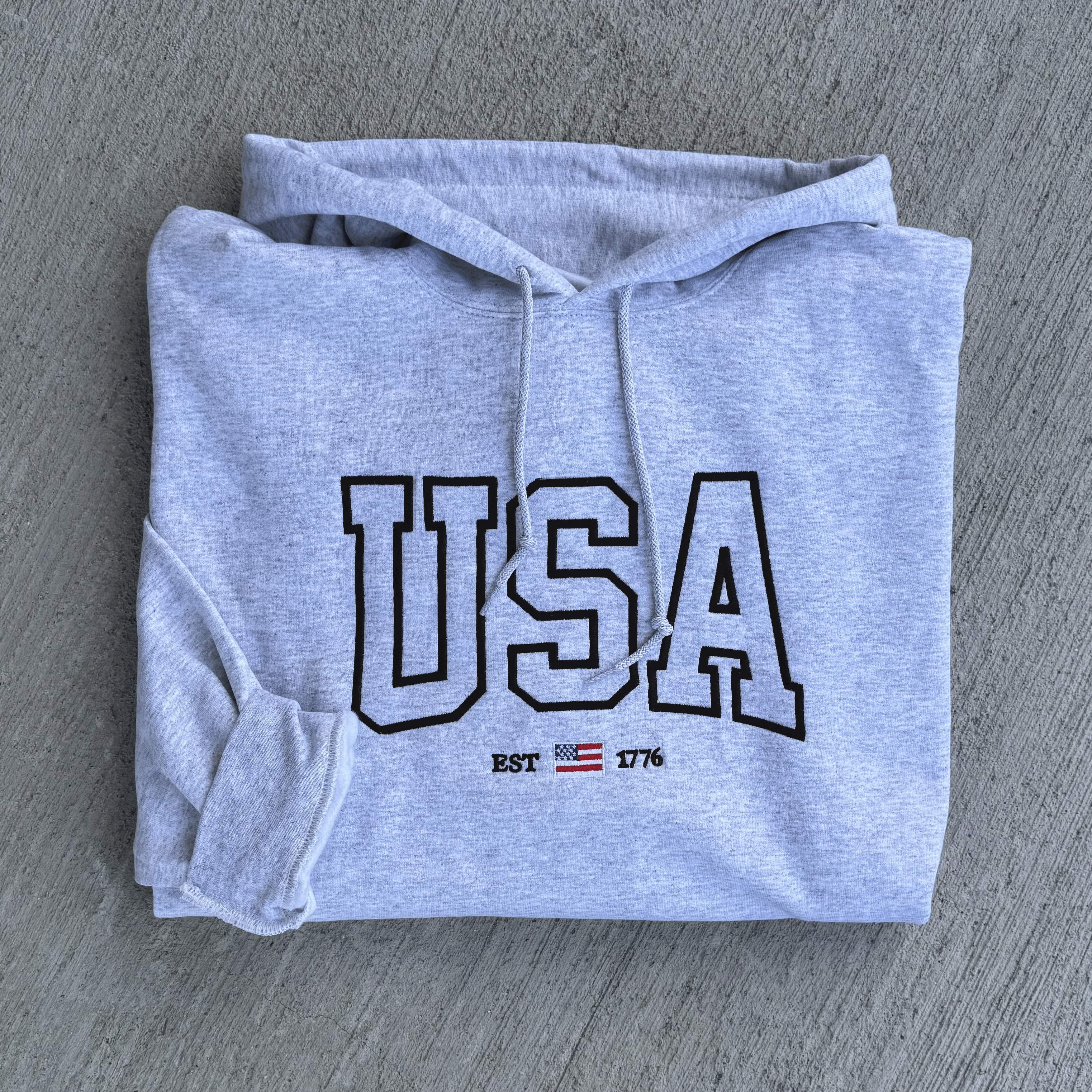 Folded gray hoodie with 'USA' text on a gray surface