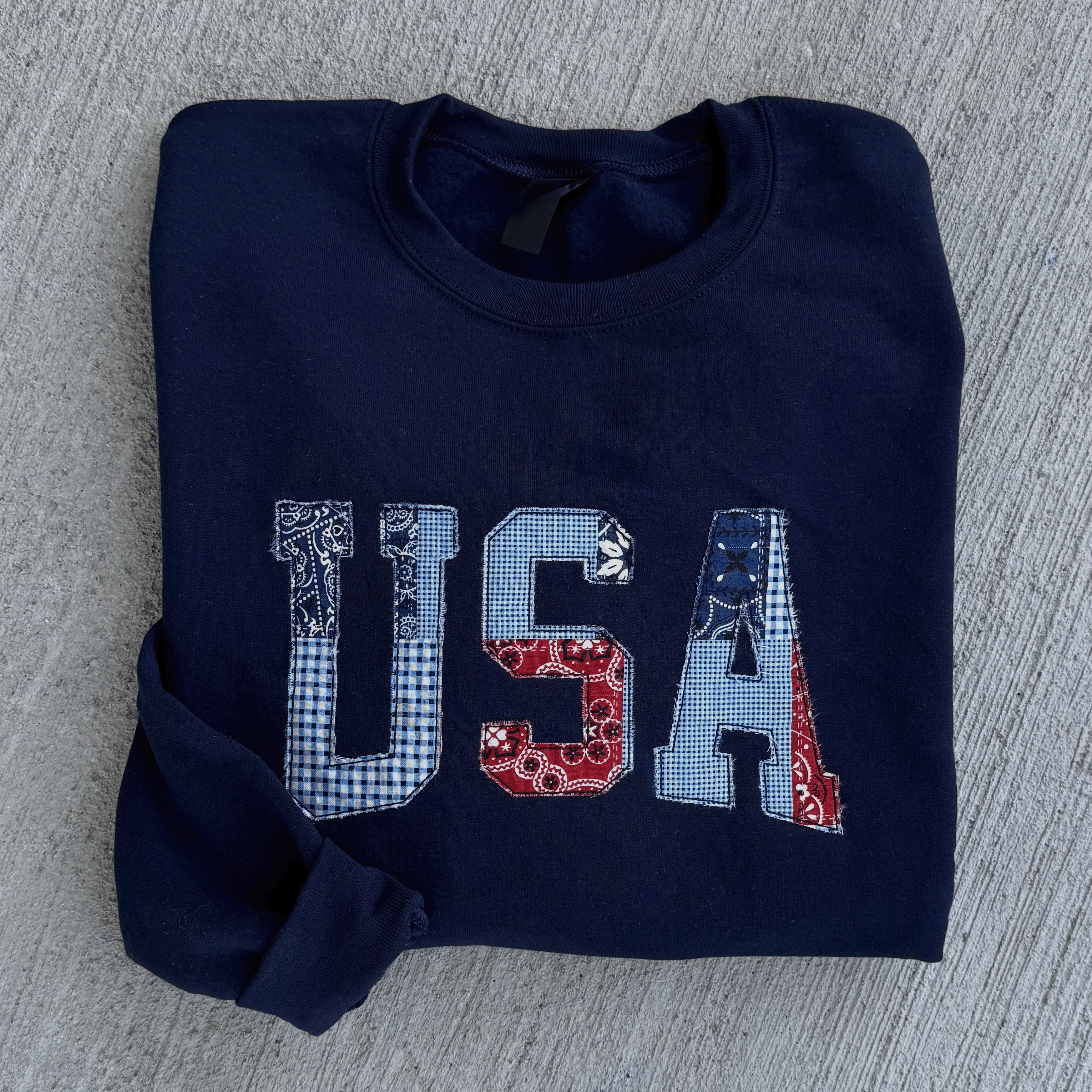Folded navy blue sweatshirt with 'USA' text on a gray textured surface
