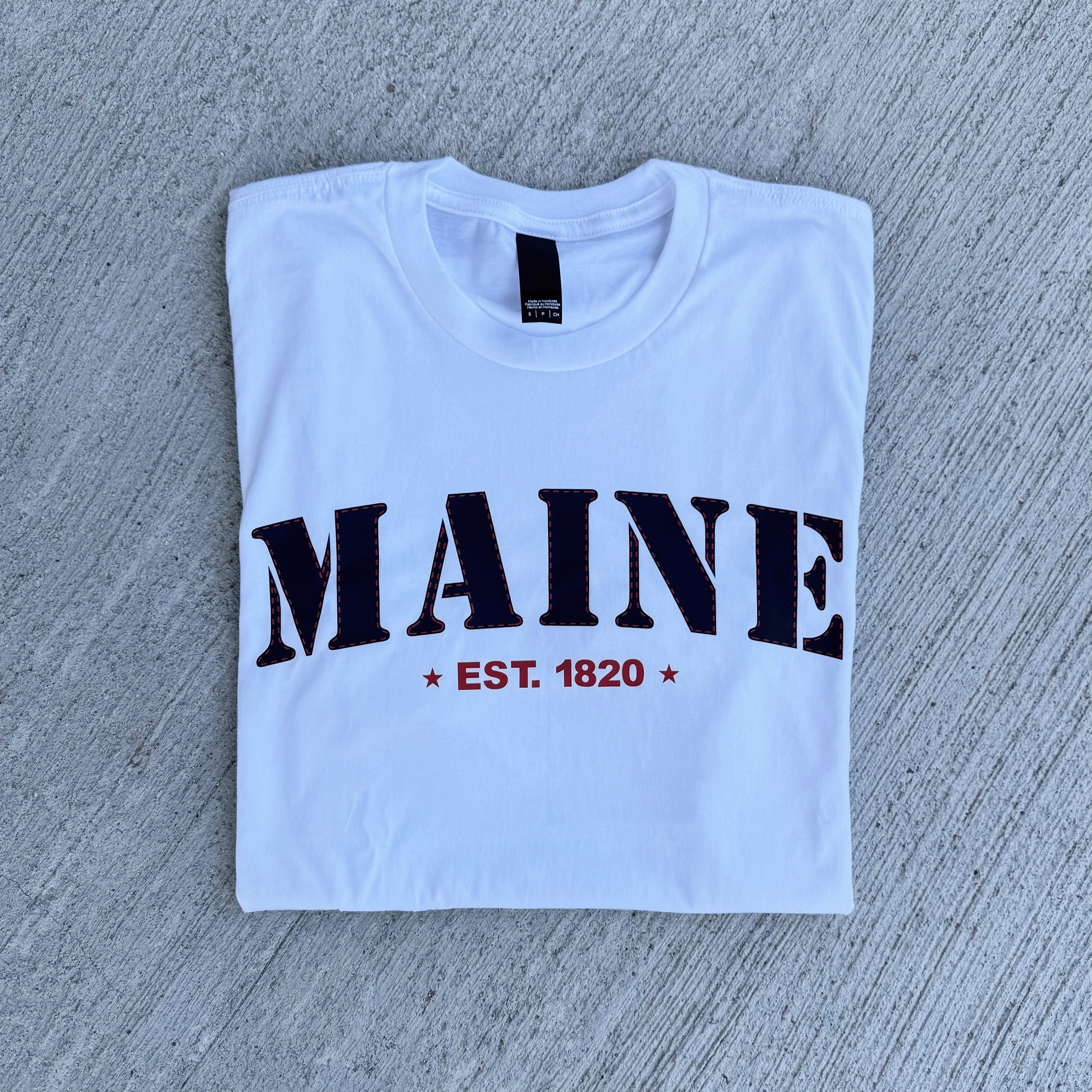White t-shirt with 'MAINE EST. 1820' text on a gray surface