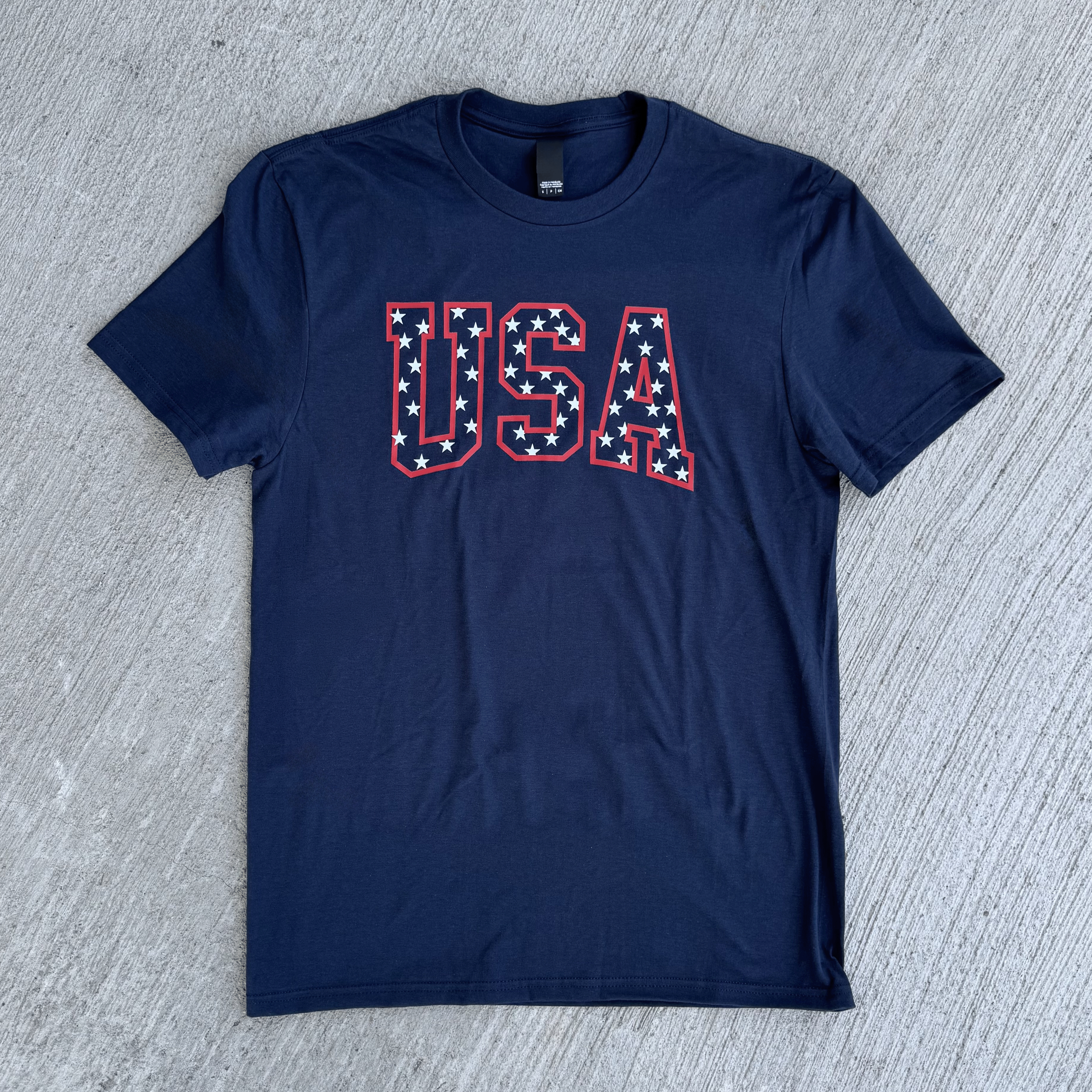 Navy blue t-shirt with 'USA' text on a gray concrete surface
