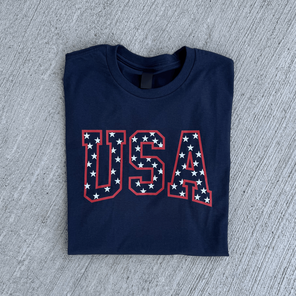 Folded navy blue t-shirt with 'USA' print on a gray concrete surface