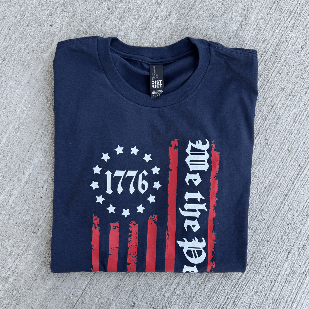 Folded navy blue t-shirt with 1776 and 'We the People' design on a textured surface