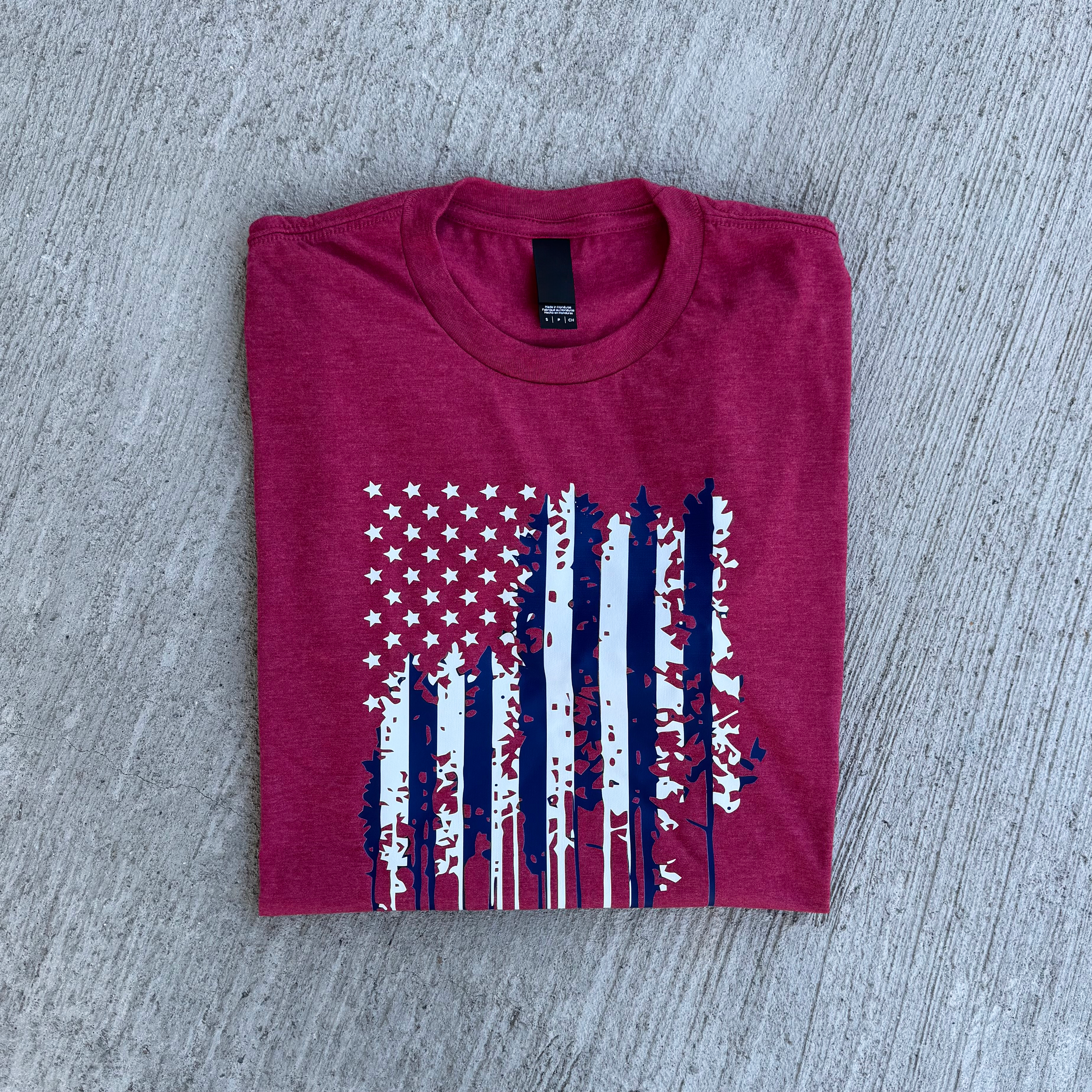 Folded heather red t-shirt with American flag design on a gray surface