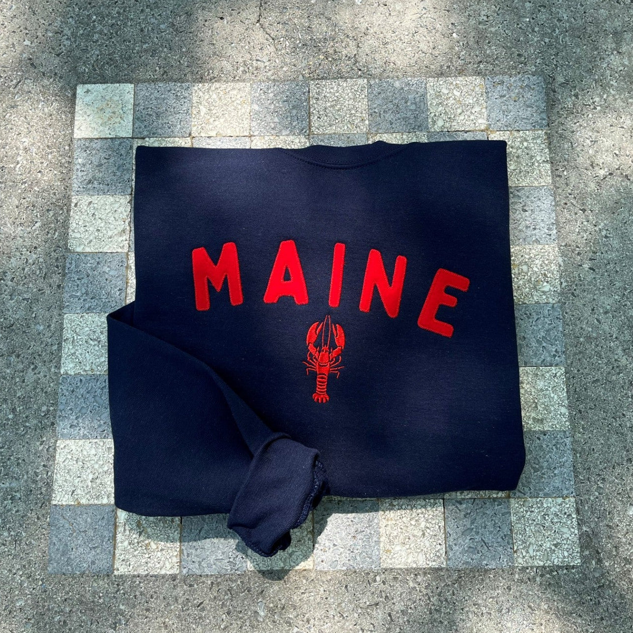 Navy blue bag with red 'MAINE' text on a stone surface